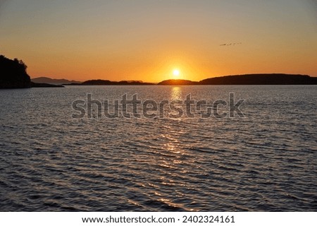 Landscape picture of the midnight sun in golden hour over the Norwegian sea with small islands at coast of northern Norway. Picture is taken from rocky beach in the arctic summer calm night.