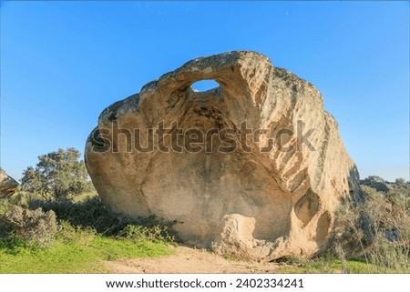 Unique granite boulder with a hole worn through revealing the blue sky with the moon in the distance