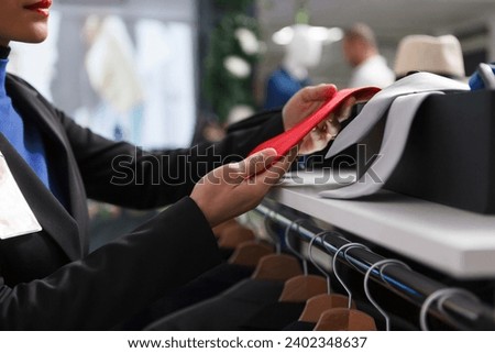 Shopping mall boutique woman worker checking trendy red tie while adjusting accessory collection on shelf. Department center clothing store employee displaying garment for sale closeup