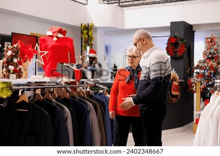 Elderly people checking belts and ties in retail store, looking at accessories to match trendy suit jacket for christmas dinner. Old couple clients searching for clothes during seasonal sales.