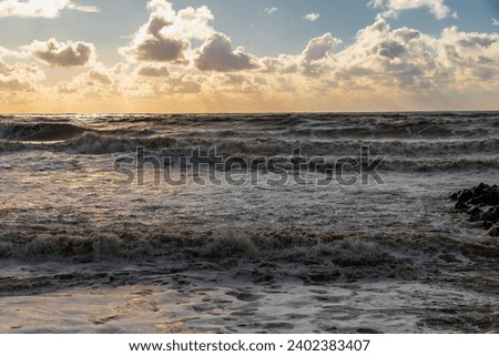 Big waves crash on the shore under a cloudy sky. An impressive sky with luminous clouds. Colorful glowing golden clouds during a storm. An epic seascape. The Black Sea during a storm. 