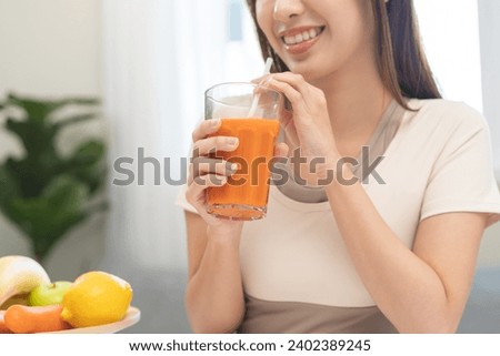 Orange detox juice concept, smile asian young woman hand holding a glass of vegetable juice, carrot smoothie for diet at home, drinking healthy meal food for weight loss. Lifestyle, vegan nutrition. Royalty-Free Stock Photo #2402389245