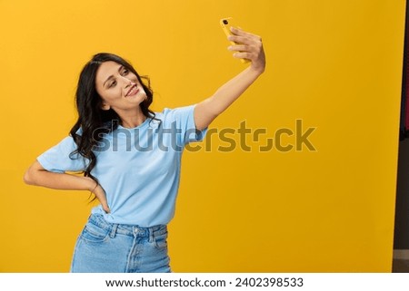 Woman blogger with a phone in her hands in a blue t-shirt and jeans on a yellow background smile signs gestures symbols, online communication and video call, copy space, free background