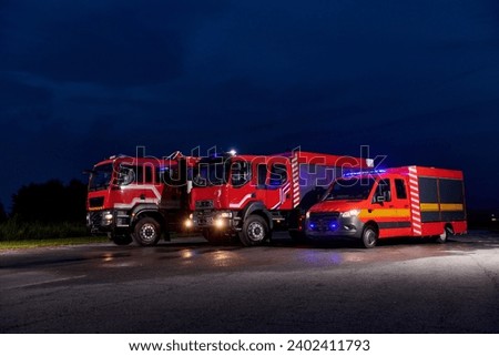 A pair of highly modern and quality fire trucks illuminate the night with their rotating lights, symbolizing the cutting-edge technology and preparedness of the firefighting fleet, ready to respond to Royalty-Free Stock Photo #2402411793