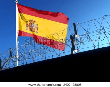 The Spanish flag hangs in a cloudy sky outside the prison's barbed wire fence. flying in the sky
