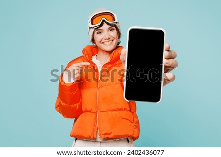 Skier young woman wear padded windbreaker jacket hat ski goggles mask use point blank screen mobile cell phone travel rest spend weekend winter season in mountains isolated on plain blue background