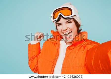 Close up winner skier young woman wears padded jacket hat ski goggles mask do selfie shot on mobile cell phone travel rest spend weekend winter season in mountains isolated on plain blue background