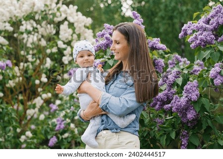 Young mother holds her baby son in her arms in a spring blooming lilac park