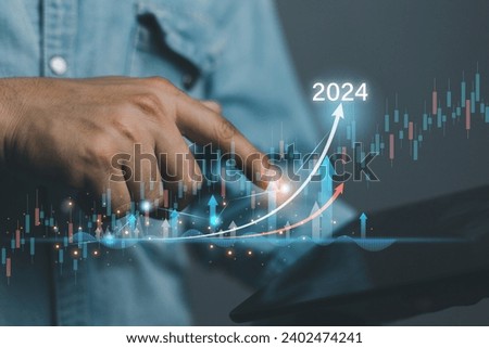 Strategy ideas  business concept. Businessman holding tablet and have futuristic graphic icon. secrete data to success in stock market on 2024. Royalty-Free Stock Photo #2402474241