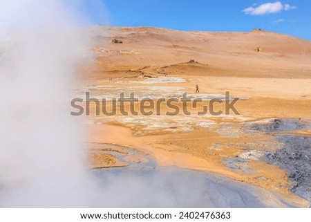 The picture captures the geothermal landscape at Hverir, Iceland, with steam plumes, orange mineral soil, bubbling mud pots, and mountainous background under a clear sky.