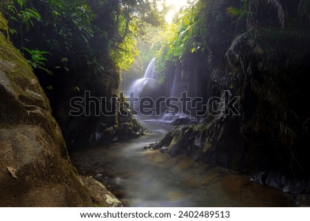 Visit the charm of Indonesia with the Lorong Watu waterfall, North Bengkulu. A narrow alley lined with stone walls, the morning light shines on the waterfall