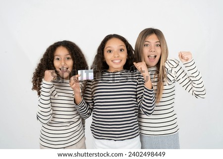 Photo of lucky impressed Three young beautiful multiracial kid girls arm fist holding credit card. Celebrated