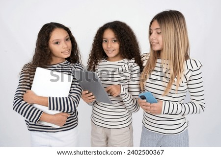 Photo of happy cheerful smart Three young beautiful multiracial kid girls hold tablet browsing internet