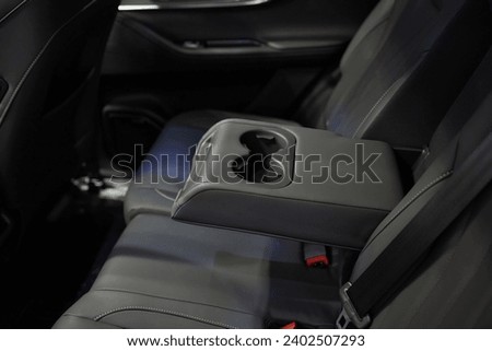 Armrest with cup holder inside. Leather comfortable white passenger seats and armrest. White leather interior of the luxury modern car. Modern car interior details. Rear passenger seats. Royalty-Free Stock Photo #2402507293