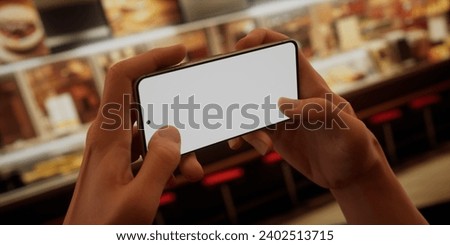 CU Photo of a person using his phone inside a fast-food restaurant. Blank white smartphone screen mock-up, food order, delivery, discount, coupon application mockup