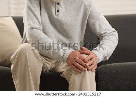 Senior man suffering from knee pain on sofa indoors, closeup. Rheumatism symptom Royalty-Free Stock Photo #2402515217