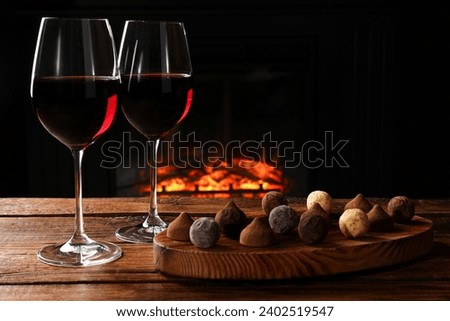 Red wine and chocolate truffles on wooden table against fireplace Royalty-Free Stock Photo #2402519547