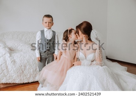 The bride is photographed with small children on the wedding day. A little girl kisses her bride on the cheek.