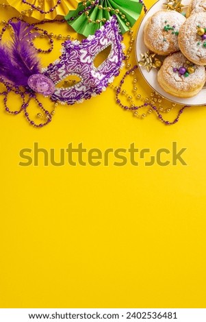 Carnival Cravings Galore: vertical top view of plate piled with scrumptious donuts, luxurious masquerade mask, colorful bead necklaces, feathers, fans on vibrant yellow setting. Feast for your senses