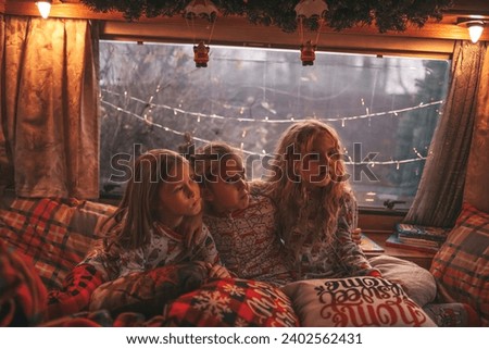 Children celebrating Christmas and New Year winter holidays season waiting Santa in camper. Kids spending time together grimace having drinks milk enjoy candy cane and cookies at Xmas camper trailer