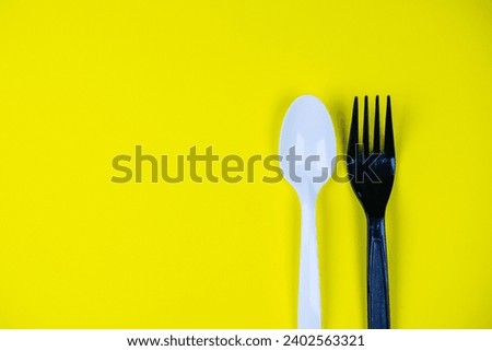 White and black plastic spoons and forks on yellow background.