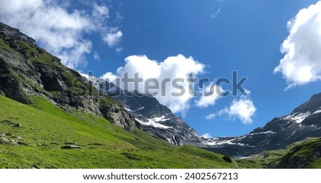 A stunning landscape featuring an expansive green hillside against a backdrop of rocky hills and a brilliant blue sky Royalty-Free Stock Photo #2402567213