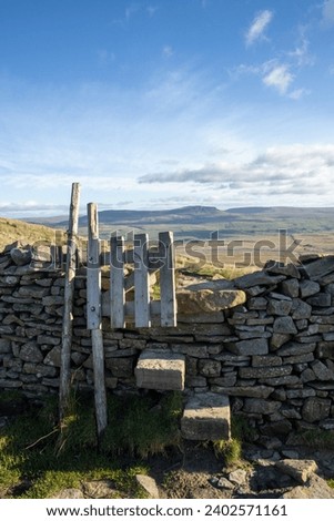 A stile in a dry stone wall in the Yorkshire Dales National Park in England, with Pen-y-ghent in the distance.

Taken on a sunny day with blue sky. Royalty-Free Stock Photo #2402571161