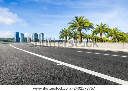 Asphalt road and green palm tree with modern buildings under the blue sky