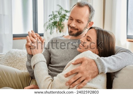 smiling child-free couple holding hands and embracing on couch in living room, warm relationship Royalty-Free Stock Photo #2402592803