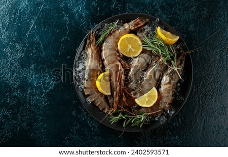 Fresh black Tiger Prawns in a black plate with lemon, rosemary and crushed ice, top view with copy space.