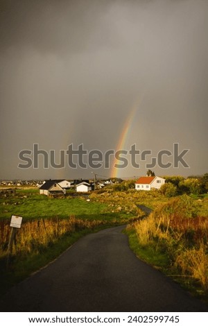 A double vibrant rainbow arching over a village with a small stream in the foreground