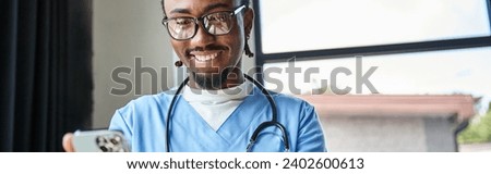 joyful african american doctor with stethoscope looking at his mobile phone, telemedicine, banner
