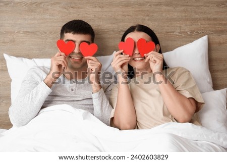 Young couple with paper hearts in bedroom