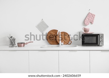 Interior of light kitchen with microwave oven, sink and utensils on white counters