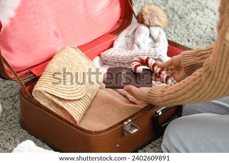 Woman holding passport and Christmas decor near suitcase with clothes, closeup