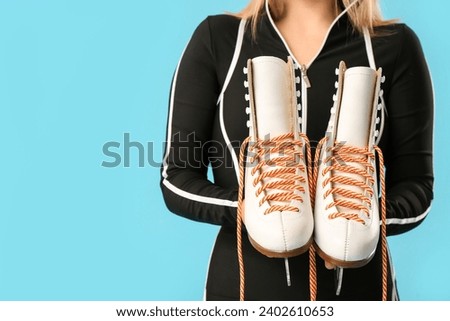Young female figure skater with ice skates on blue background