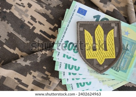 Ukrainian army symbol and bunch of euro bills on military uniform. Payments to soldiers of the Ukrainian army from European union, salaries to the military. War support to Ukraine