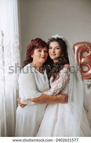 A beautiful and happy mother and her daughter, the bride, are standing next to each other. The best day for parents. Tender moments at the wedding. Royalty-Free Stock Photo #2402631577