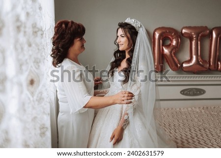A beautiful and happy mother and her daughter, the bride, are standing next to each other. The best day for parents. Tender moments at the wedding. Royalty-Free Stock Photo #2402631579