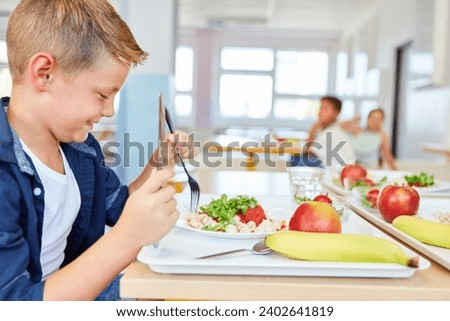 Happy schoolboy eating meal with cutlery while sitting at table in cafeteria Royalty-Free Stock Photo #2402641819