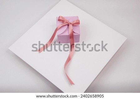 A picture of a pink present, wrapped in a white ribbon bow, on a crisp white background