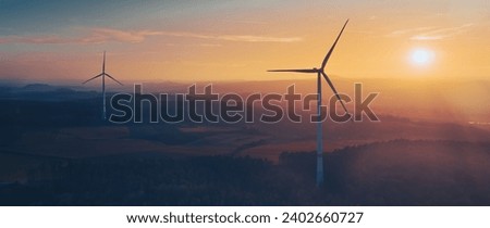 Three wind turbines are silhouetted against a vibrant orange and pink sunset sky, providing a stunning visual of renewable energy