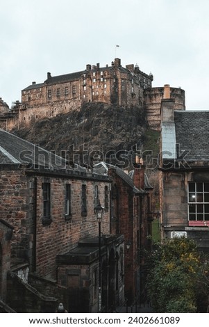 A picturesque view of an old cobblestone alleyway in Edinburgh, Scotland with Edinburgh Castle in the background.
