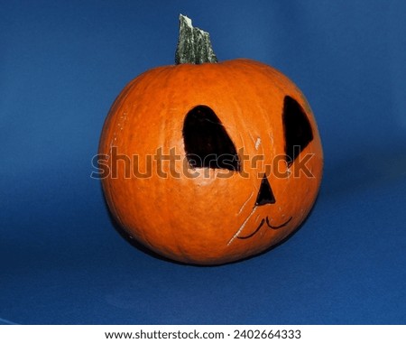 On a dark blue background stands an orange round pumpkin with a nose and mouth drawn in black. side view . Halloween. copy space