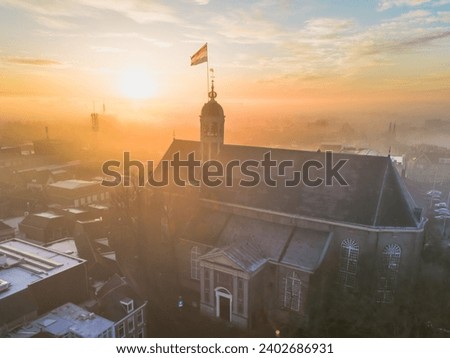 Drone view across town of Sneek with Dutch flag on top of a church at sunrise