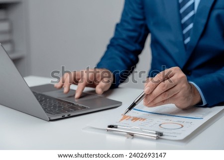 Close-up of a businessman hand pointing business data graph and using laptop computer at workplace.