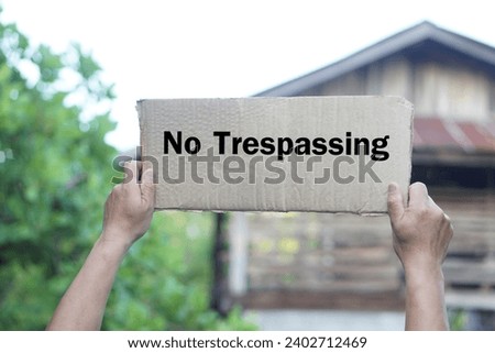 Close up hands holds No Trespassing sign, paper card in front of house. Concept, private property security, privacy, and protection for trespassing . Warning.                            