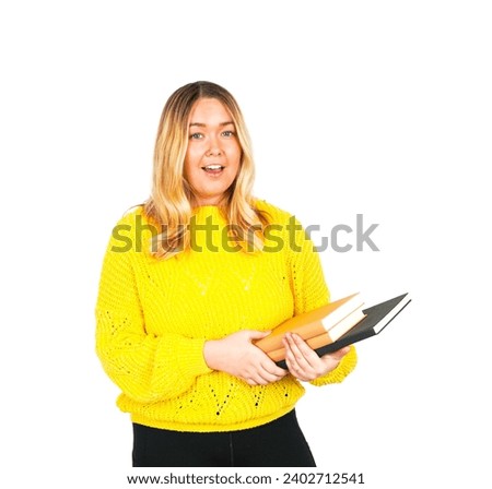 Happy young blonde teacher smiling while holding books and wearing a yellow jumper against a white background