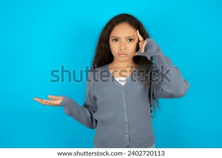 Young beautiful teen girl confused and annoyed with open palm showing copy space and pointing finger to forehead. Think about it.