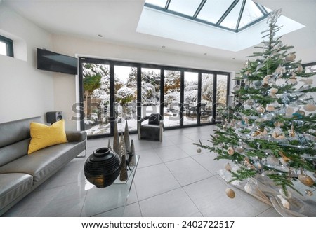 Bifold doors and skylight at Christmas in luxury room, Xmas tree and view to garden with snow. Royalty-Free Stock Photo #2402722517
